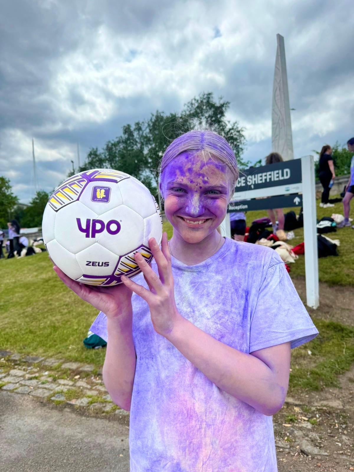 A schoolgirl covered in powdered paint holding a YPO-branded football.